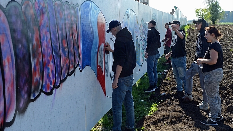 Gemeinsame Arbeit der Hausemer Jugendlichen am Graffiti auf der Abschrankung der Baustelle Törlenmatt. (Bild Bernhard Schneider)
