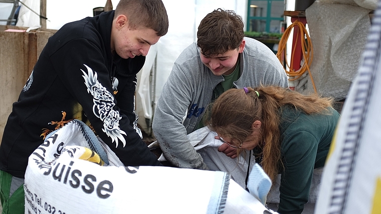 Drei junge Erwachsene mit einem geschützten Ausbildungsplatz im Götschihof der Solvita-Stiftung arbeiten beim Abmischen der Gartenerde zusammen. (Bild Salomon Schneider)