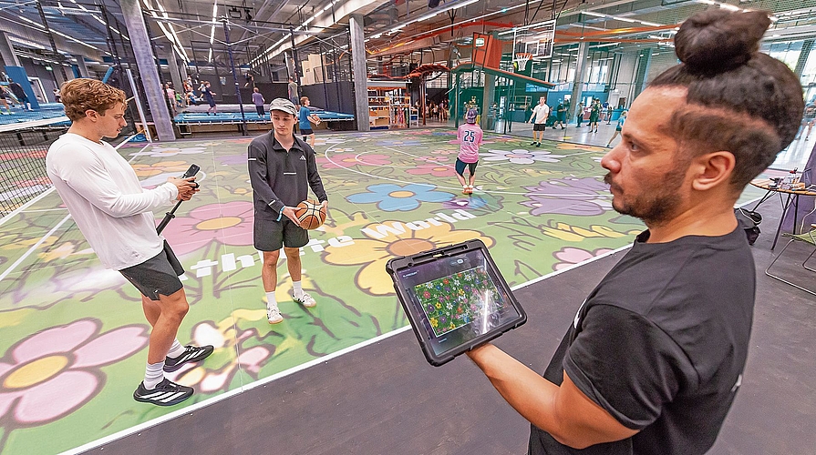Weltweit erstmals auch für die Öffentlichkeit buchbar: ein ASB-Glassfloor. Innerhalb von wenigen Sekunden kann beispielsweise von einer Basketballfeld- auf eine Volleyballfeld-Begrenzung umgestellt werden. Gleichzeitig kann die Spielfläche mit x-beliebigen Sujets versehen werden (hier ein Blumenmuster). Athlete-World-Co-Geschäftsführer Nehemiah Sousa (rechts) benötigt dafür lediglich ein Tablet. (Bilder Daniel Vaia)