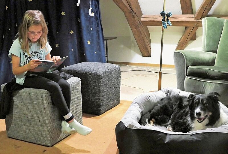 Jana Trächslin setzt sich auf einen Hocker und liest Lesehund Mojito konzentriert vor. Später wechselt sie an den Rand des Bettes, um dem Hund näher zu sein. (Bild Regula Zellweger)
