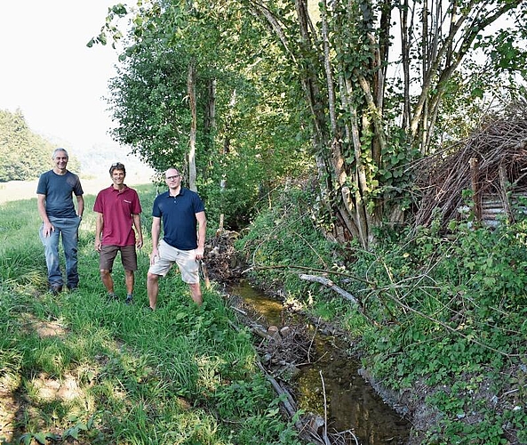 Sie freuen sich über das gelungene Projekt, hier mit Asthaufen am Ufer und Bachverengungen mittels Holz und Steinen. 
Von links: Umweltvorstand Ruedi Taverna, Andreas Nagel von «Rundum Natur» und Tiefbauvorstand Sven Kammer. (Bilder Marianne Voss)