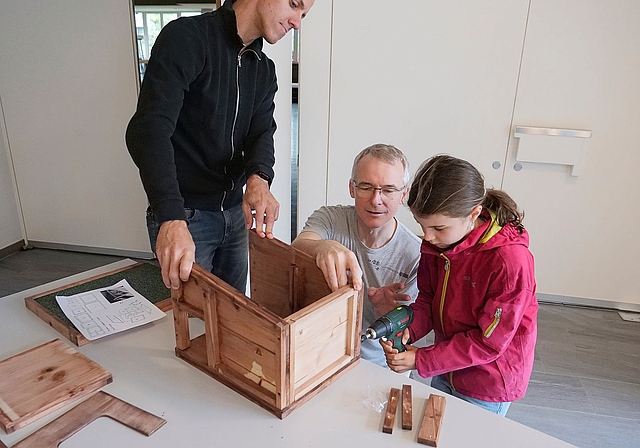 Jörg Strohmeier (m.) schraubt mit Aria und ihrem Vater ein Igelhaus zusammen.