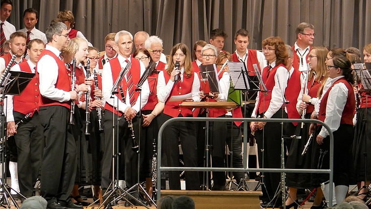 Wenn zwei Musikvereine auf der Bühne Platz finden müssen, bleibt kein Platz für Stühle. In der Mitte mit Mikrofon: Katja Krauer, die den Anlass mit viel Charme moderierte. <em>(Bild Regula Zellweger)</em>