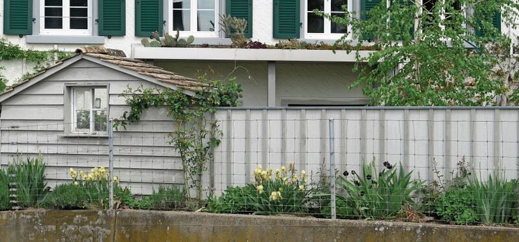 Von der Dorfstrasse her ist der Garten geschützt. Mit der Blumenrabatte und dem integrierten Häuschen vermittelt er einen freundlichen Eindruck.