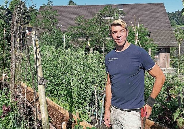 Hanspeter Leder ist bereit für Garten-Taten. Im Hintergrund weisen Fähnchen zum erntebereiten Gemüse. (Bild Sandra Claus)