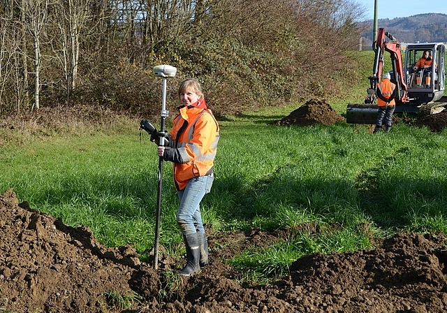 Grabungsleiterin Stefanie Brunner mit dem GPS-Gerät, das Fundstellen auf wenige Zentimeter genau markiert. Im Hintergrund beobachtet ihre Kollegin Adina Wicki den Aushub des Baggers an einer zweiten Sondierungsstelle. (Bild bs)