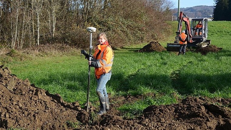 Grabungsleiterin Stefanie Brunner mit dem GPS-Gerät, das Fundstellen auf wenige Zentimeter genau markiert. Im Hintergrund beobachtet ihre Kollegin Adina Wicki den Aushub des Baggers an einer zweiten Sondierungsstelle. (Bild bs)
